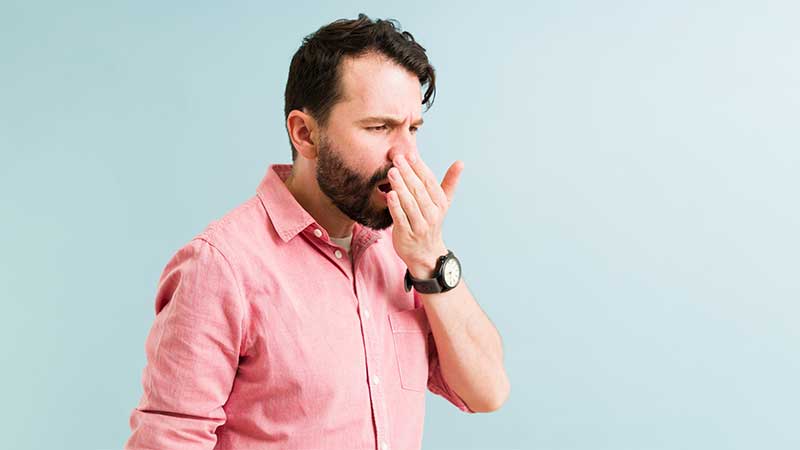 Homem a verificar o hálito colocando a mão esquerda à frente da boca aberta